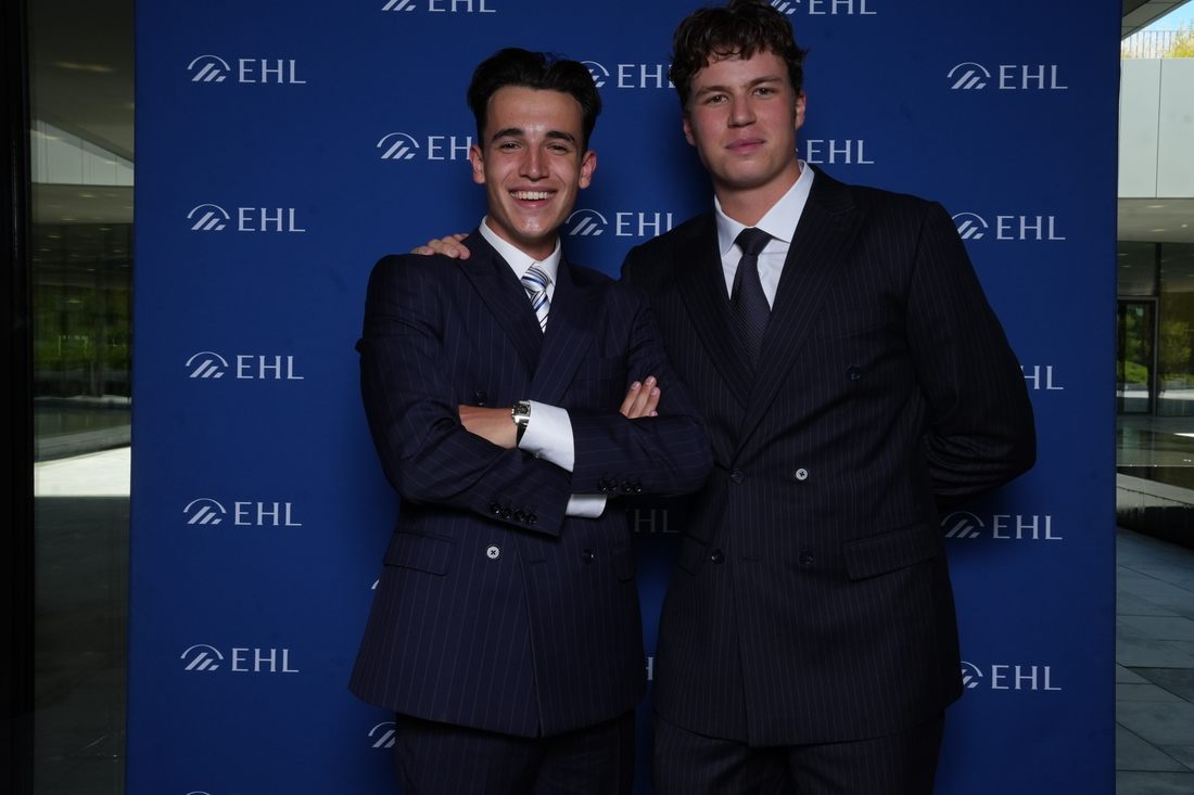 The two founders of Serimont in navy pinstripe suits, photographed in front of an EHL backdrop in Lausanne.