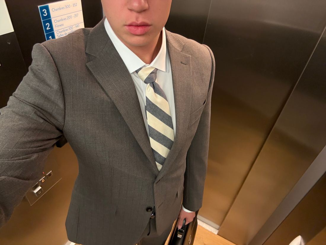 Grey pinstripe single-breasted suit with notch lapels, worn with a white shirt and a cream and grey striped tie.