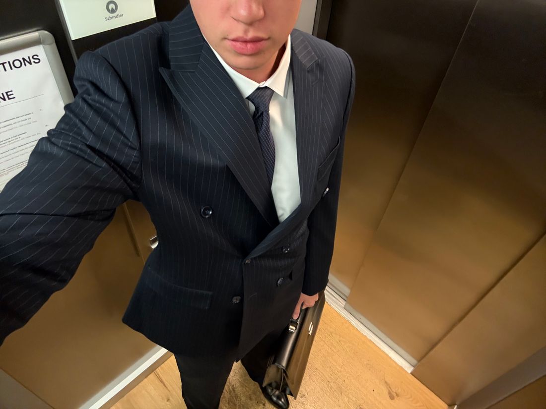 Navy pinstripe double-breasted suit with peak lapels, worn with a white shirt and a dark tie.
