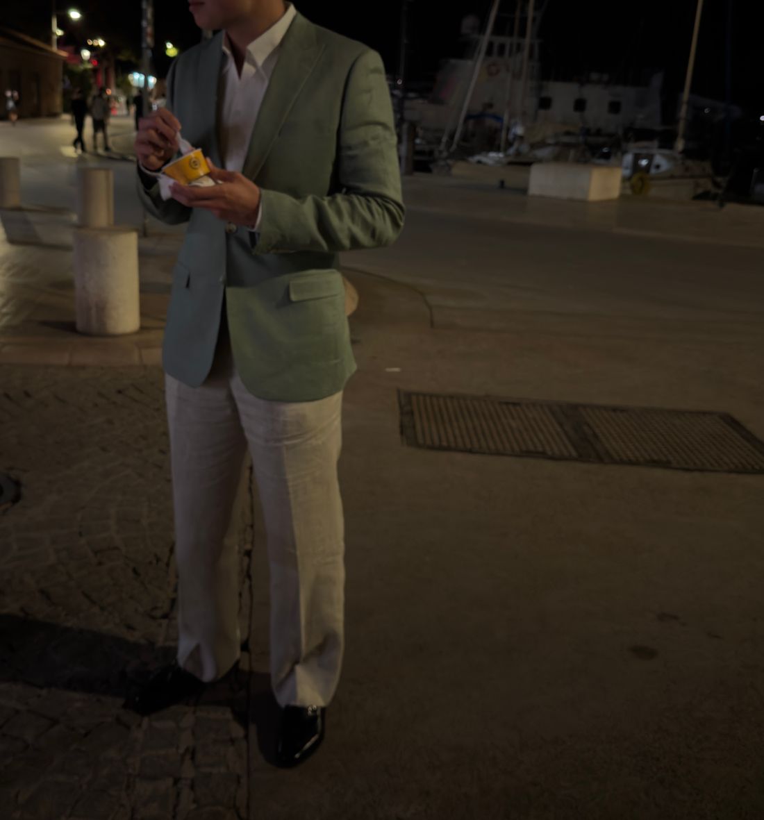 Sage linen jacket worn open over a white shirt with ivory linen trousers and black leather shoes.